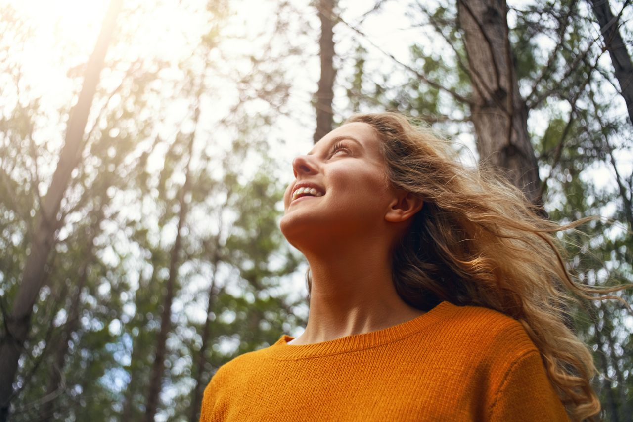 Eine junge Frau lächelt und genießt den Sonnenschein in einem Wald